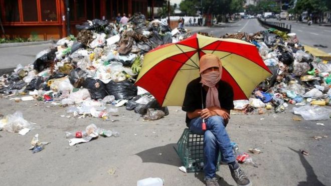 متظاهر ملثم يجلس بجوار كوم من القمامة